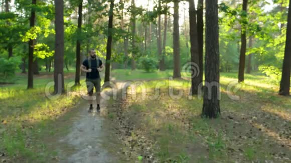 一个带背包的留着胡子的人沿着森林的小路走着身后夕阳西下旅途自然慢动作视频的预览图