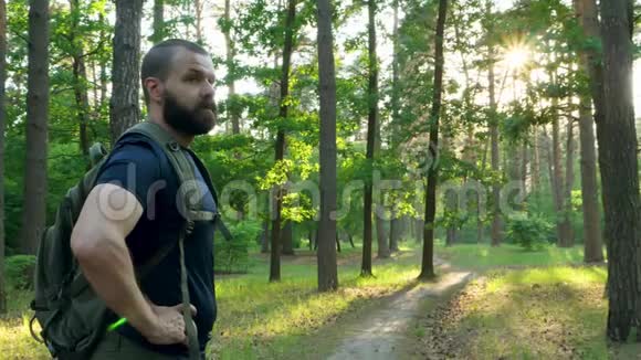 一个带背包的留胡子的人站在树林里环顾四周那个人开始沿着森林小径散步相机在移动视频的预览图