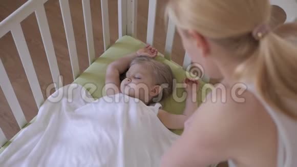 母亲抚摸一个熟睡的孩子的手产妇护理婴儿正在婴儿床上休息视频的预览图