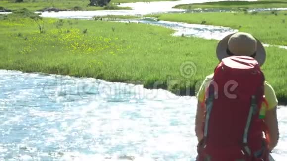 那个带着红色背包的旅行者女人坐在河岸上山区视频的预览图