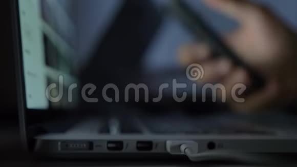 模糊的特写镜头手与智能手机在笔记本电脑前面的黑暗背景视频的预览图