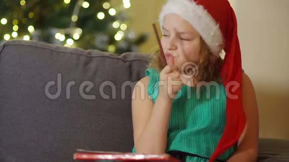 一个穿着优雅的绿色连衣裙戴着圣诞帽的女学生坐在圣诞树旁手里拿着一支铅笔青少年视频的预览图
