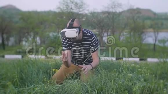 一个戴着虚拟现实眼镜的人坐在城市公园的草地上视频的预览图