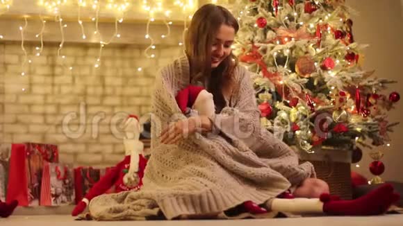 有格子的年轻女子坐在圣诞树旁边微笑着手里拿着圣诞老人玩视频的预览图