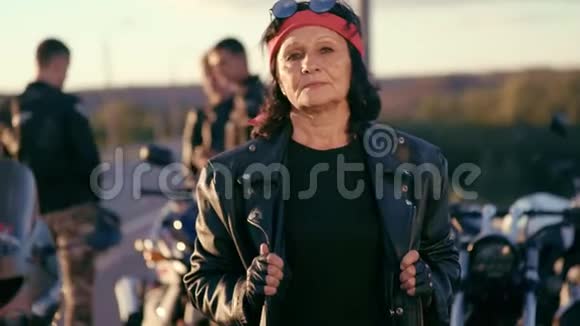 一位身穿红手巾皮夹克和手套的老妇人站在年轻人陪伴的背景下视频的预览图