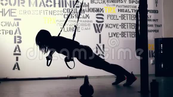 在光线的背景下一个黑暗的身影一个穿着紧身裤和上衣的女人的轮廓在TRX环上锻炼视频的预览图