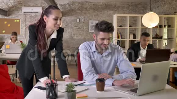 两个年轻的商人正在交谈在办公室里看着图形和笔记本电脑与技术联网工作视频的预览图