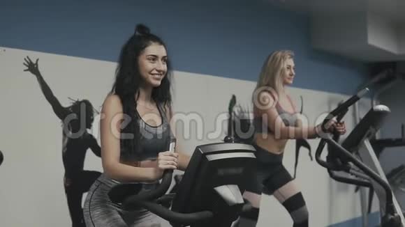年轻的健身妇女穿着运动服在椭球上做运动在健身房骑自行车视频的预览图