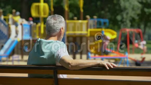 男性退休老人坐在长凳上在操场上看孙子家人视频的预览图