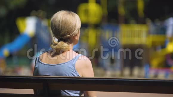 悲伤的老女人坐在操场上的长凳上看着孩子不孕视频的预览图