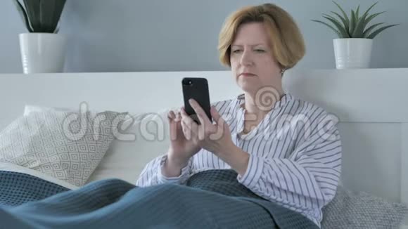 高龄老人躺在床上使用智能手机视频的预览图