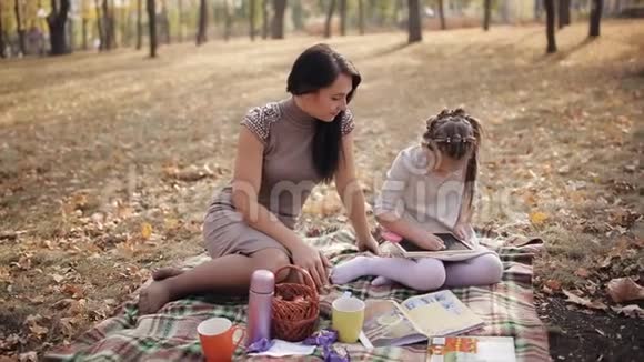 一位年轻的母亲正在抚养一个女儿小女孩用粉笔在黑板上画画家庭假期视频的预览图