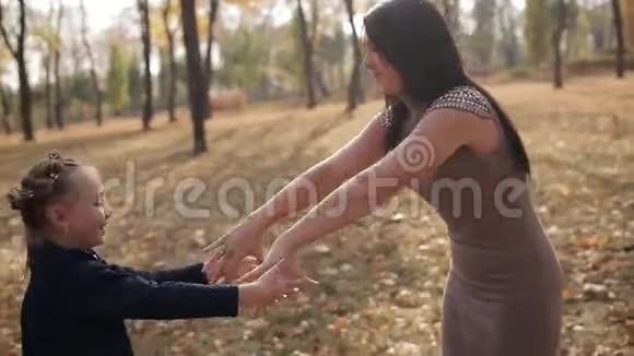 一位年轻的母亲正在一个秋天的城市公园里把她的女儿围起来一个幸福的家庭视频的预览图