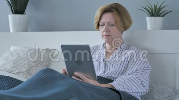 躺在床上使用平板电脑的老年妇女视频的预览图