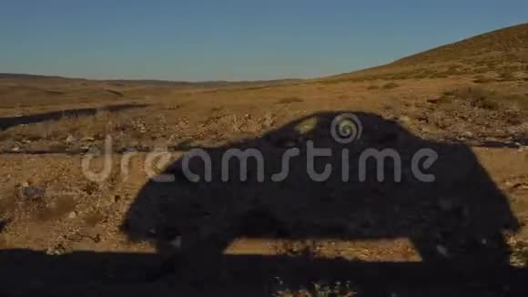 日落时分一辆汽车在宽阔的荒地景观中行驶在乡间的道路上视频的预览图
