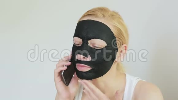 一个脸上戴着黑色抗衰老化妆面具的女人在打电话视频的预览图