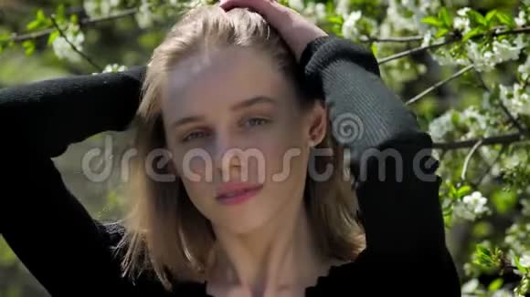 年轻迷人的女孩在夏天的白天在公园摸头发在镜头前看在背景上开花视频的预览图