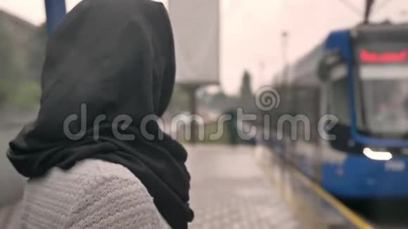 戴着头巾的年轻穆斯林妇女正在观看火车下着雨宗教观念交通观念天气视频的预览图