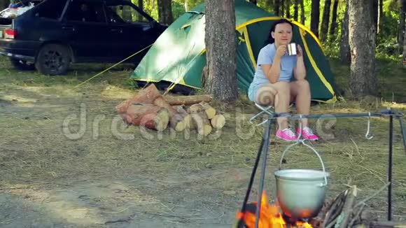 一个年轻的女人在帐篷附近喝茶看着一个保龄球挂在火上视频的预览图
