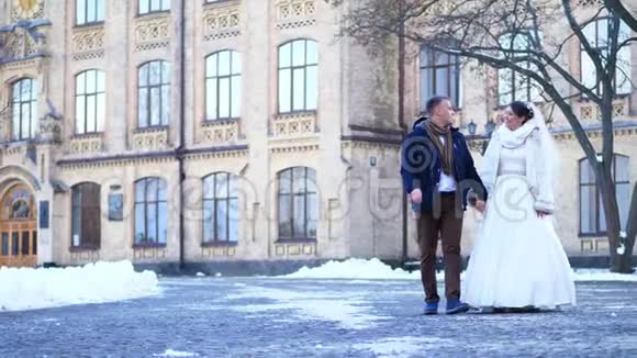 冬季婚礼新婚夫妇穿着婚纱走在白雪覆盖的公园里背景是视频的预览图