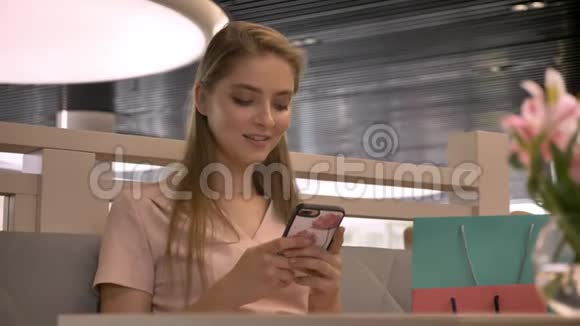 年轻漂亮的女孩坐在rastaurant在智能手机上聊天喝咖啡微笑看着相机视频的预览图