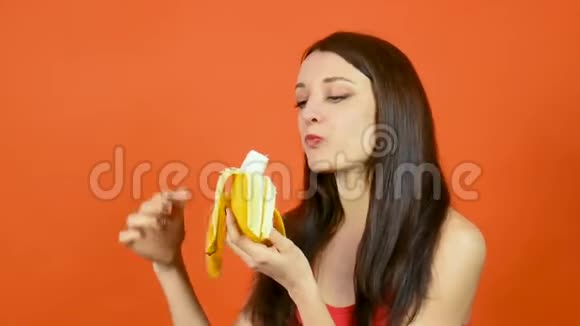 有趣的年轻饥饿妇女吃香蕉在明亮的橙色背景热带水果减肥理念视频的预览图