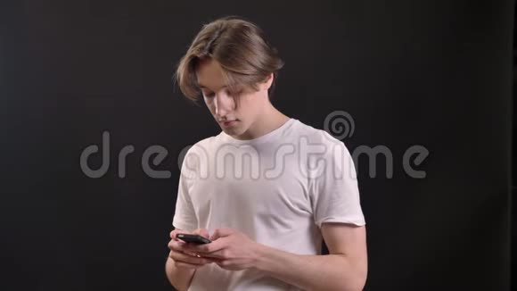 年轻的迷人男子穿着白色衬衫拿着电话看着摄像机在黑色背景下被隔离视频的预览图