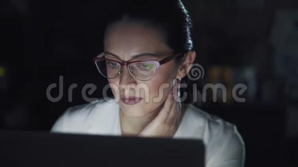 戴着眼镜的商务女性在黑暗的办公室里用笔记本电脑工作视频的预览图