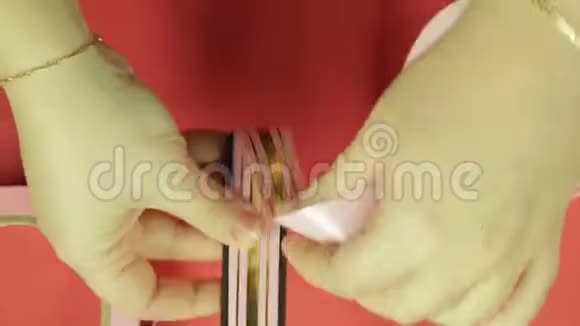女人手正在模板上包裹一条粉红色的丝带用来做礼物蝴蝶结红色背景视频的预览图