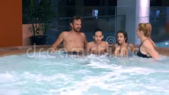 幸福的家庭在户外按摩浴缸放松两个十几岁的孩子一个女人和一个男人在游泳池附近的热水里放松视频的预览图