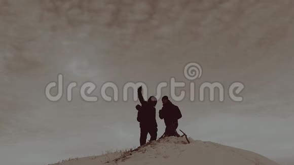 登山者两个背着背包的旅行者的剪影向对方展示了冬季登山时的相机视频的预览图