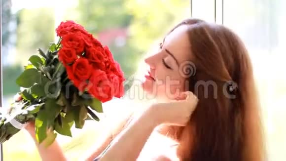 美丽的女人特写微笑着嗅着红玫瑰花的香气视频的预览图
