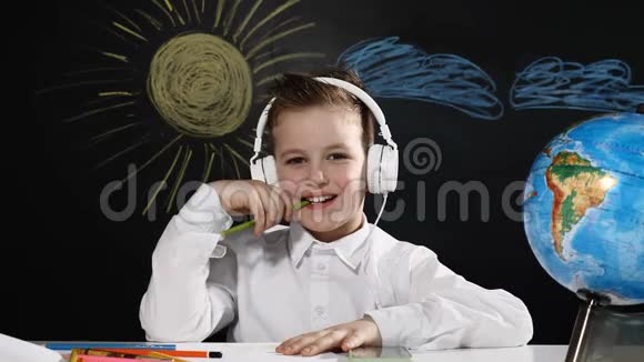 学校观念拇指向上可爱的男孩坐在一张桌子上桌子上有地球仪后面有一块黑板微笑的小学生视频的预览图