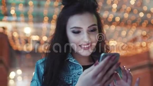 旋转观看美丽的黑发女孩使用她的手机和微笑的屏幕在俱乐部入口处夜总会视频的预览图