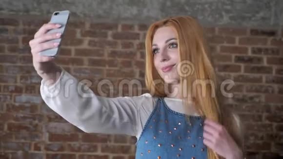 年轻可爱的金发女孩正在智能手机上自拍微笑砖背景沟通理念视频的预览图