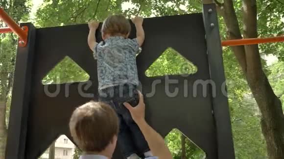年轻的父亲把他的小儿子放在脖子上在公园里跳着绿树夏天视频的预览图