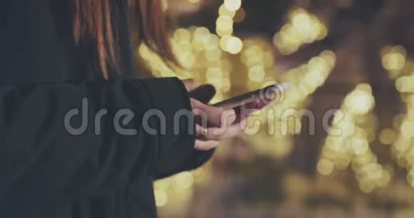 女人在城市黄昏时用智能手机夜间路灯背景模糊视频的预览图