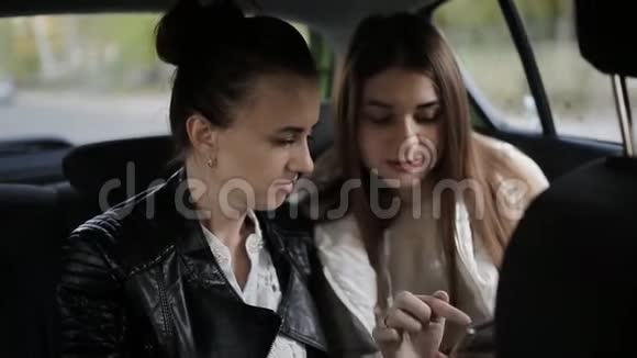 两个女人坐在坐出租车的汽车后座说话和使用智能手机视频的预览图