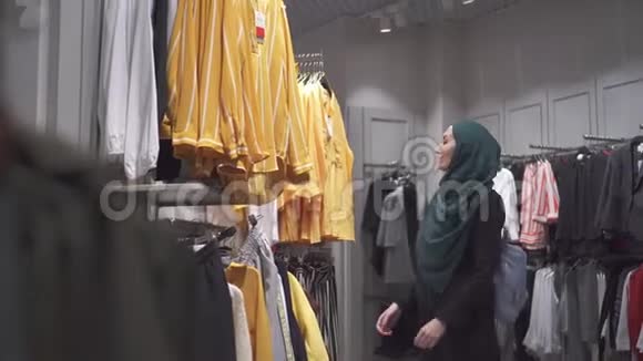 年轻漂亮的穆斯林女人戴着头巾和背包在商店里挑选衣服视频的预览图