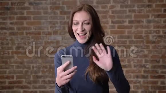 棕色头发的女孩在智能手机上用视频聊天交流概念砖背景视频的预览图