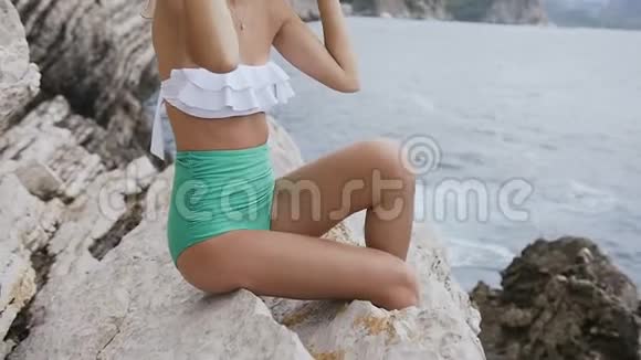 戴着帽子和泳衣的年轻女子坐在岩石上看着黑山彼得罗瓦茨的亚得里亚海有魅力的女孩视频的预览图
