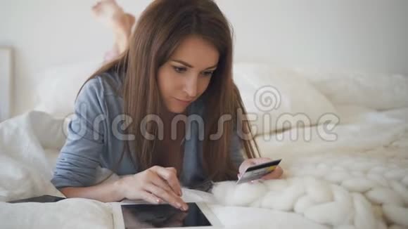年轻女子躺在床上用信用卡在平板电脑上购物视频的预览图