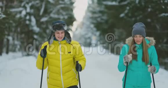 冬天一个穿黄色夹克的男人和一个穿蓝色连衣裙的女人在树林里慢动作滑雪视频的预览图