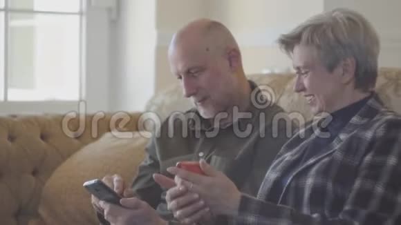 一对成年夫妇坐在大沙发上秃头男子在手机上为他的成熟女人展示照片她个子矮小视频的预览图