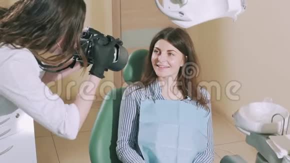 漂亮的闪亮女孩坐在牙科椅上对着镜头微笑一个假人被一个牙医拍照以添加视频的预览图