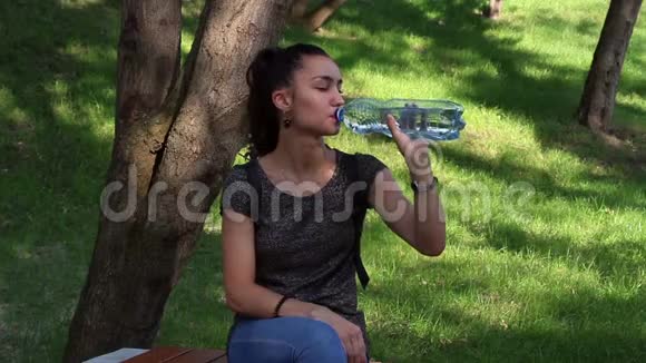 年轻漂亮的女孩打开一个塑料瓶里面放着水喝着她的水视频的预览图