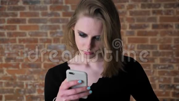 一个眼睛冒烟的年轻女孩正在看智能手机上的照片震惊交流理念砖背景视频的预览图