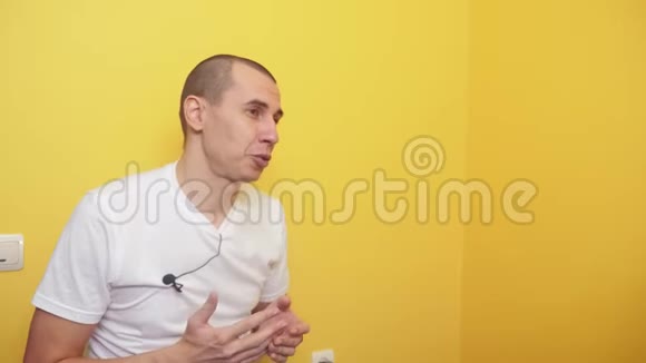 博客人的概念男子录制视频与麦克风扣眼在t恤上黄墙背景生活方式视频的预览图