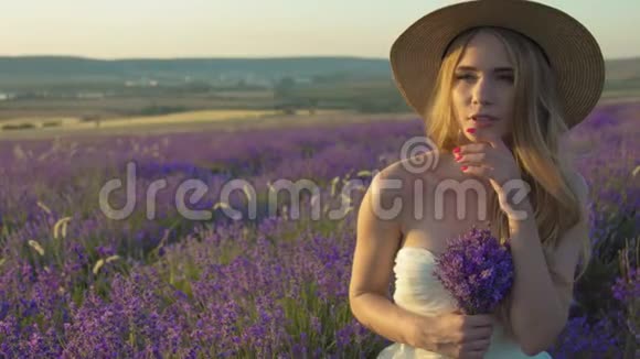 美丽的年轻女子戴着草帽在夕阳下的田野里享受着薰衣草的芬芳视频的预览图