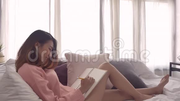 慢动作美丽的年轻亚洲女人在家里的卧室里放松时躺在沙发上看书的肖像视频的预览图